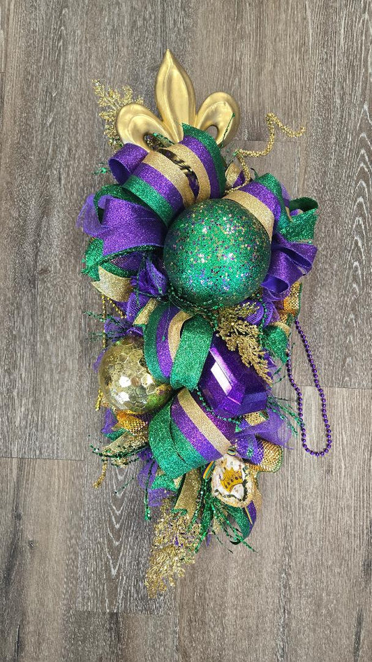 Decorative wreath with green, purple, and gold ribbons and beads on a wooden background